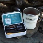 Outdoor setting with a 'Uncharted' branded mug and a small kit on rocks.