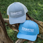 Two 'Uncharted' branded hats on a wooden branch with grass background